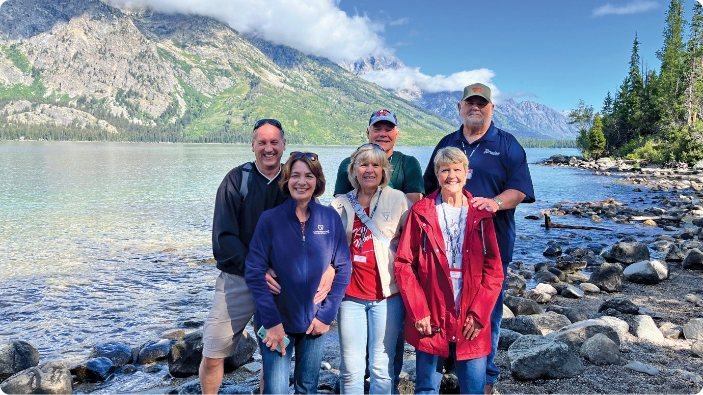 A group of Holiday Vacations travelers standing standing in a scenic view of a lake and mountain